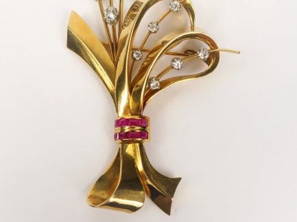 Broche en or jaune à décor d'un ruban orné d'un pavage de petits rubis