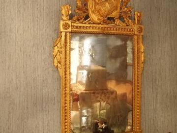 Glace Louis XVI en bois et stuc doré, fronton à décor de drapeaux et d