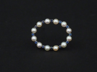 Vente aux enchères Broche ovale en or blanc, sertie de pierres bleues et perles blanches 