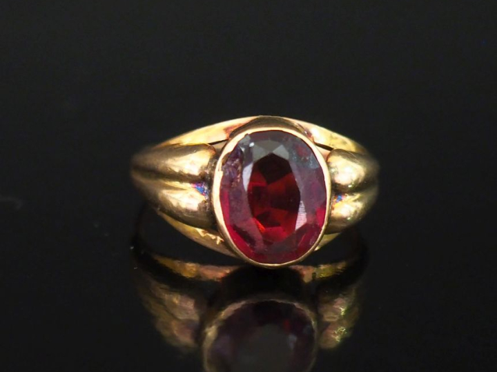 Bague en or jaune 750, sertie en son centre d'une pierre rouge.  La mo