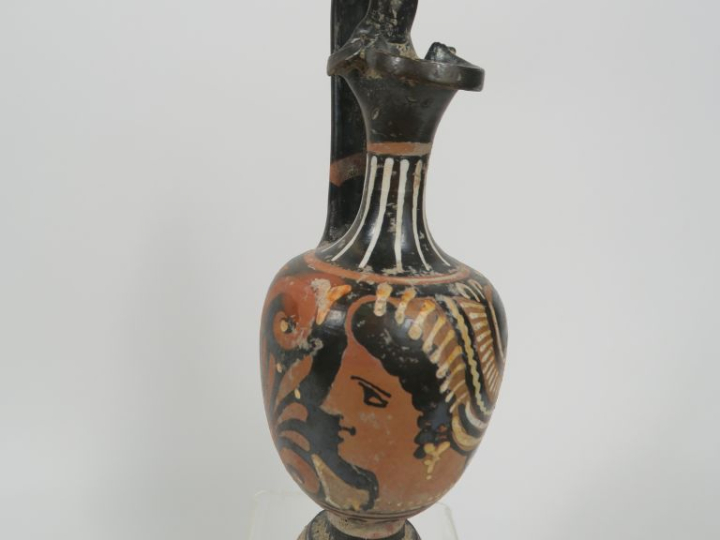 Vase grec. Œnochoé à figures rouges décorée d’une tête féminine et de 