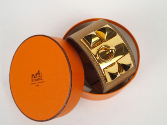 Vente aux enchères HERMES. Bracelet manchette en métal doré et cuir étoupe, modèle "Médor