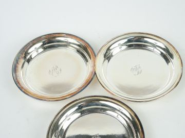 Suite de trois dessous de bouteilles en métal argenté. Monogrammés