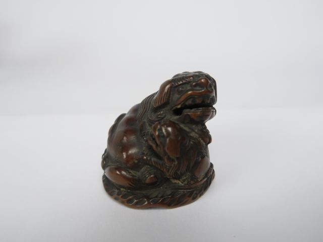 Netsuke en bois représentant un shishi assis, la patte posée sur son p