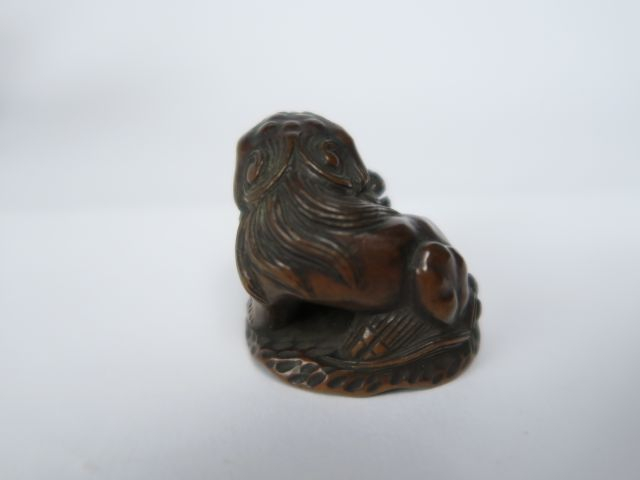 Netsuke en bois représentant un shishi assis, la patte posée sur son p