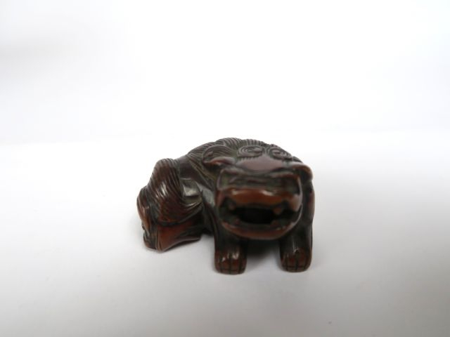 Netsuke en bois représentant un shishi couché, tenant une balle mobile