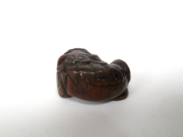 Netsuke en bois représentant un shishi couché, tenant une balle mobile