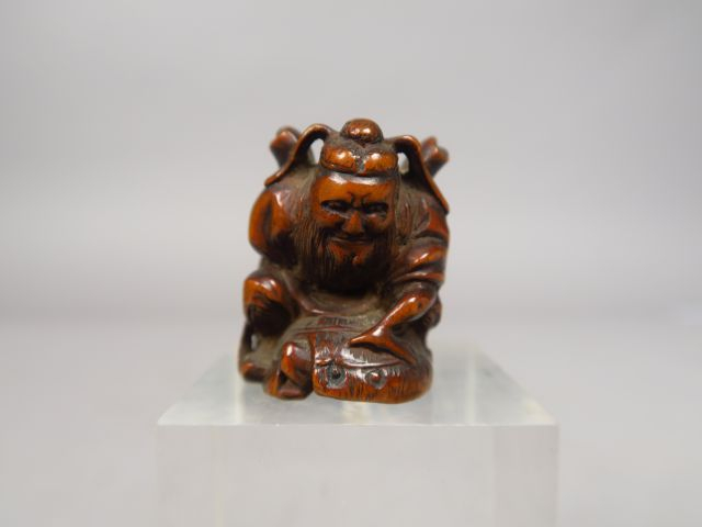 Netsuke en bois représentant Shoki plaquant au sol un grand chapeau so