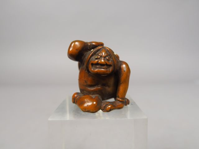 Netsuke en bois représentant un oni assis, retenant de sa main droite,