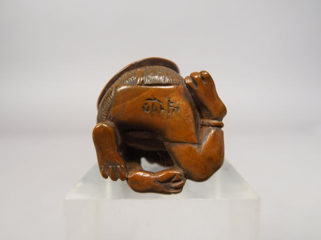 Netsuke en bois représentant un oni assis, retenant de sa main droite,