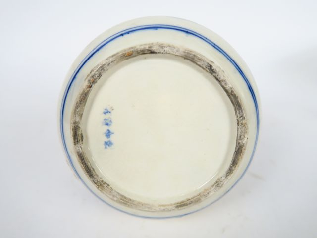 Bouteille en céramique bleu sur fond crème, décor de paysage lacustre.