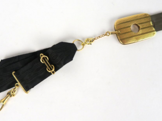 Vente aux enchères 	Coupe-cigarillos en or et métal, sur son lien en soie noire. Poids te