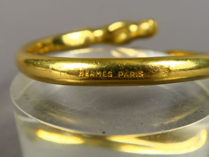 HERMES.  Bracelet jonc en métal doré, à décor de chevaux.  Signé.