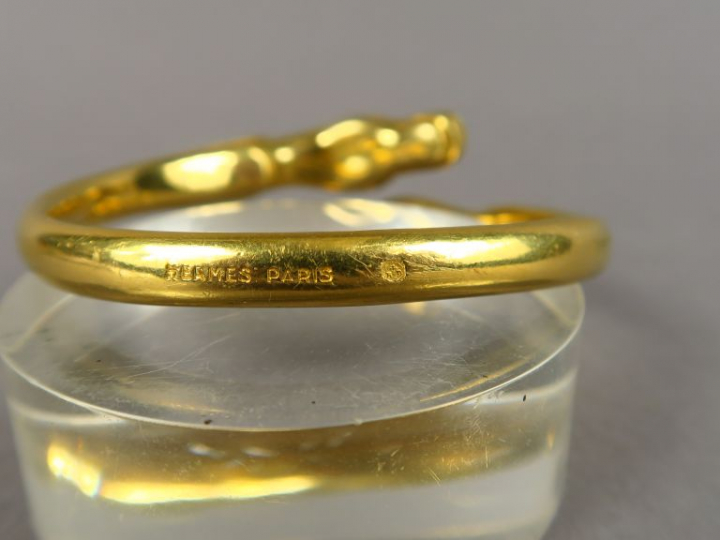 HERMES.  Bracelet jonc en métal doré, à décor de chevaux.  Signé.