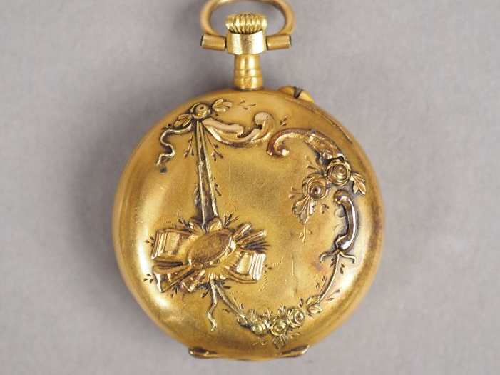 Montre de col en or jaune.  Le revers à décor de trophée d'instruments