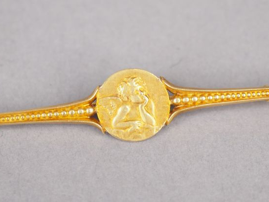 Broche en or jaune, ornée d'un petit médaillon à décor d'amour. Long. 