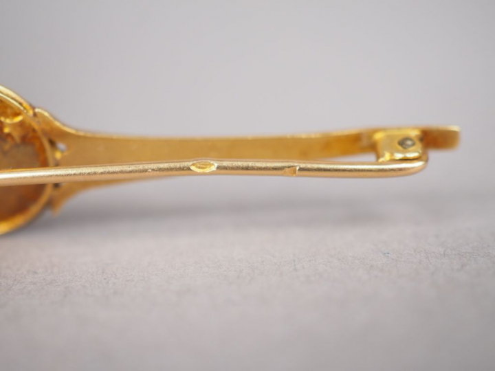 Broche en or jaune, ornée d'un petit médaillon à décor d'amour. Long. 