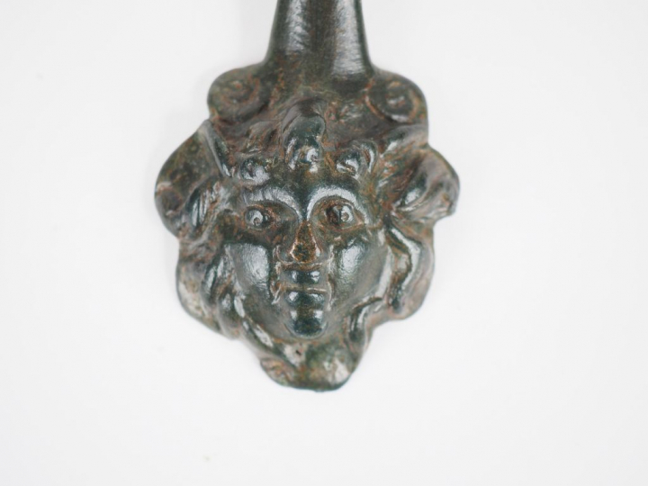 Anse en bronze avec un visage en médaillon. Epoque romaine. L. : 16 cm