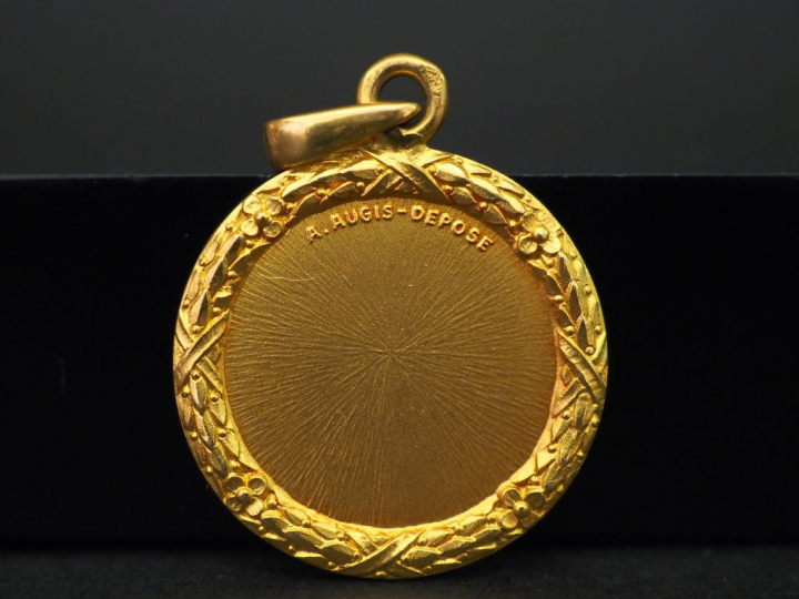 Médaille en or jaune, marquée « + qu’hier - que demain », sertie de ci