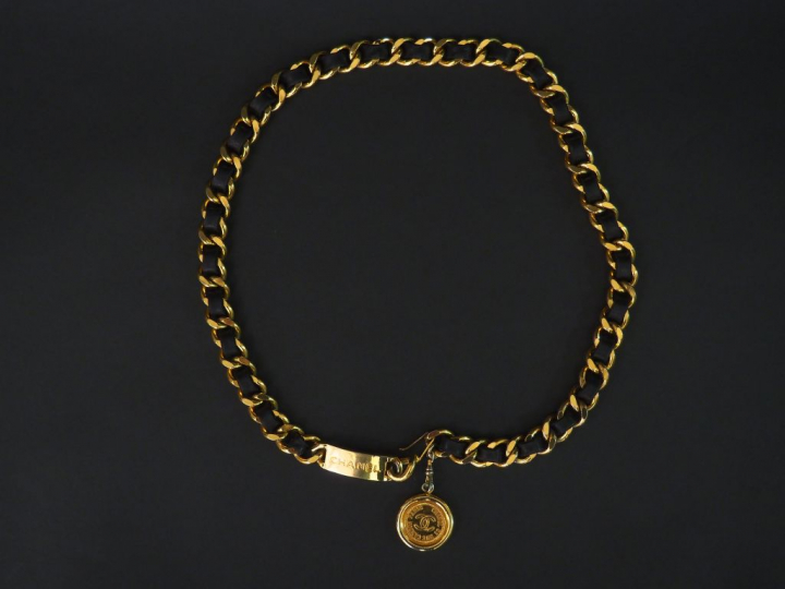 CHANEL. Ceinture en métal doré entrelacé de cuir noir, à médaille grif