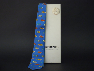 Vente aux enchères 	CHANEL Cravate en soie bleue, à décor polychrome de voitures. Signée.