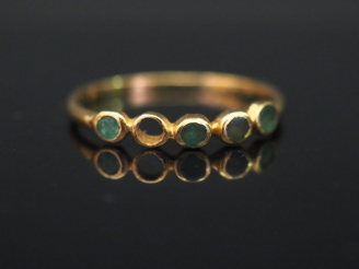 Vente aux enchères Petite bague en or jaune, sertie d’une ligne de quatre pierres vertes.