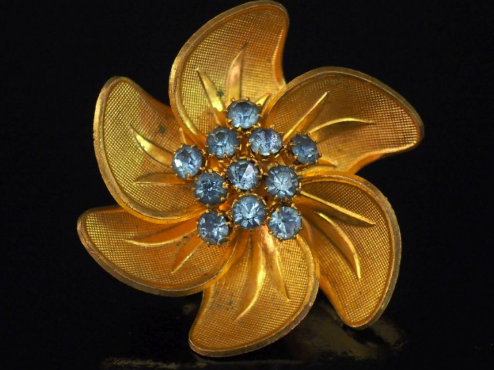 Broche en métal doré et pierres fantaisie bleu ciel en forme de fleur.