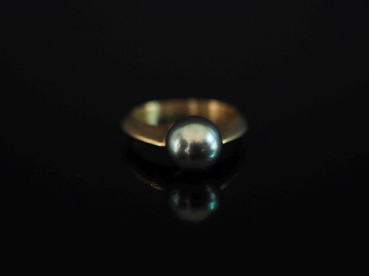 Bague en or jaune 750, sertie en son centre d'une perle grise.  TDD. 5