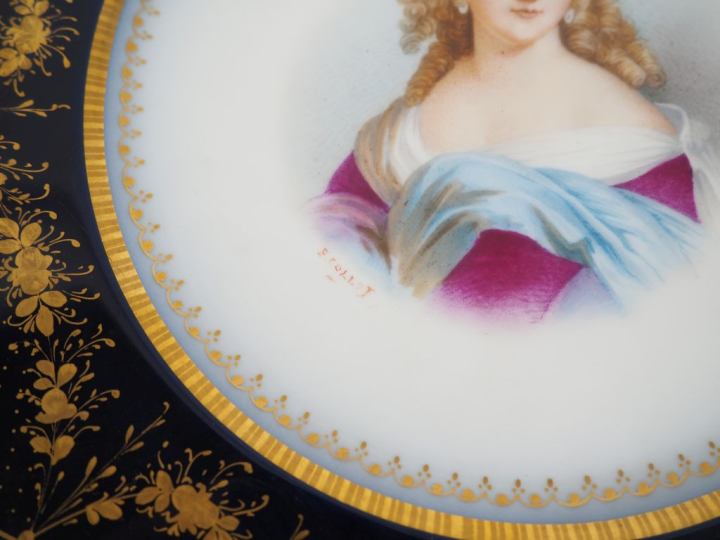 SEVRES.  Assiette en porcelaine à décor polychrome de jeune fille. Sig