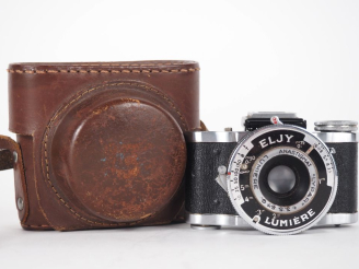 Vente aux enchères ELJY LUMIÈRE. Appareil photographique miniature avec étui.